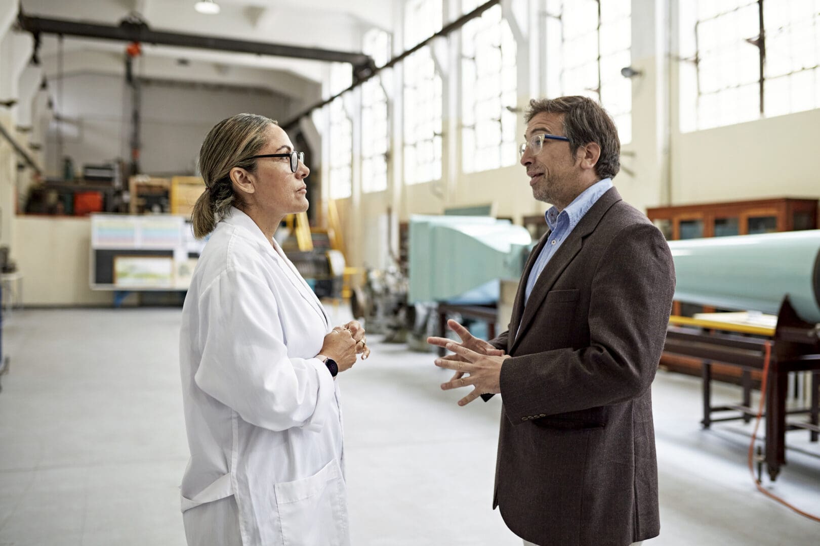 Male college professor standing face to face and conversing with late 40s woman in lab coat as they exchange ideas. Property release attached.